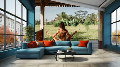 Young woman practicing yoga duringyoga retreat in Asia, Bali. Sit in lotus pose, Meditation, relaxation, getting fit, green grass jungle background. Terraced rice field in rice season in Bali Wall mural