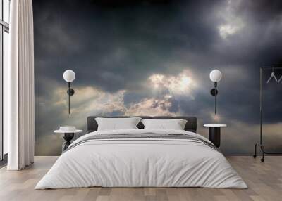 The sky was covered with dark rain clouds and beams of light streaked through the clouds. Wall mural