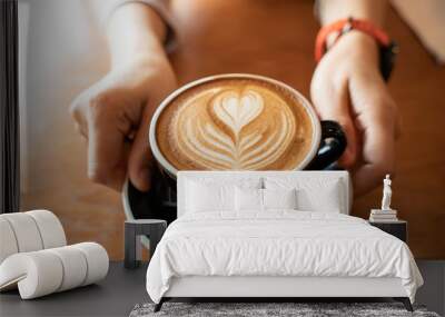 Close up Cup of coffee latte in coffee shop.Female hands holding a cup of coffee cup with heart shaped latte art foam on black wood table. Wall mural