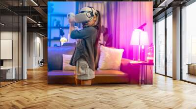 Girl 6 y.o. experiencing VR headset game at home.daughter wearing VR eyeglasses on the metaverse,Child playing metaverse gaming gadget for virtual reality,goggles at home.Virtual technology concept. Wall mural