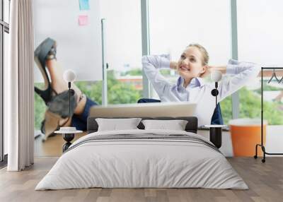 Portrait of a relaxed young businesswoman sitting with legs on desk in a bright office.Happy business colleagues in modern office using labtop. Wall mural