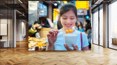 Asian young female eating famous street food - fish ball, in Hong Kong Wall mural