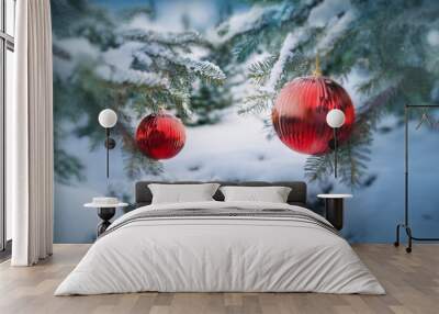 Two red ornaments hang from a snow-covered evergreen tree branch, a winter wonderland scene. Wall mural