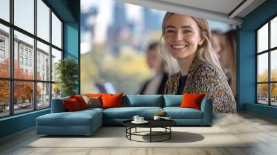 A vibrant and engaging seminar in action, with a focus on a smiling woman at the forefront, exuding confidence and leadership. Business team gathered in a modern meeting room. Wall mural