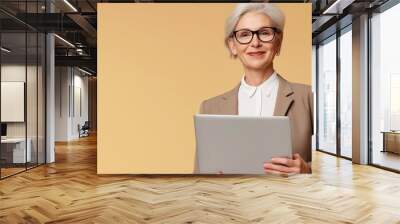 Happy mature business woman using laptop standing isolated on beige background. Middle aged professional businesswoman ceo executive holding computer. Wall mural