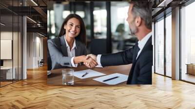 Happy professional mature Latin businessman and businesswoman wearing suits shake hands sitting at table having partnership business contract agreement. generative AI Wall mural