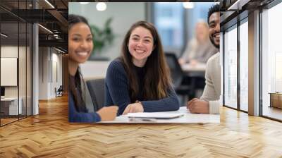 Three diverse young professionals sitting at an office table, smiling and having a meeting. Wall mural