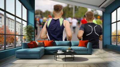 Young men in sportswear running marathon in city, wireless earphones in their ears, other contestants on blurred background. Runners at sports competition Wall mural