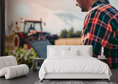 Modern agriculture concept with a farmer analyzing data on a laptop with a tractor in the background Wall mural