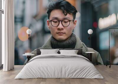 Young adult in glasses focused on his phone amidst urban backdrop Wall mural