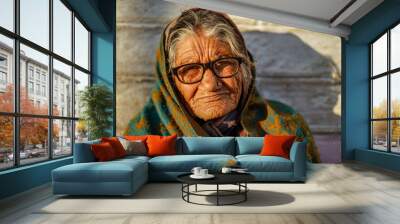 Old aged woman sitting with the support of the wall in the sunset wearing glasses Wall mural