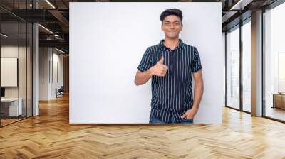 young good looking man wearing a half shirt showing thumps up looking into the camera standing a white background Wall mural