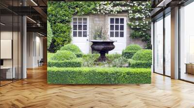 Flower vase in green topiary garden in front of a stone English country house, with two patio doors surrounded by white flowering climbing plant . Wall mural