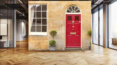 Red wooden doors in an old traditional English stone cottage with two plant pots in front . Wall mural