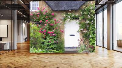 White wooden doors in Cotswold charming stone cottage with pink and red roses climbing the wall . Wall mural