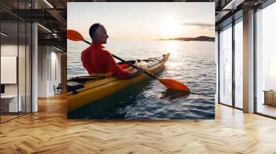 Senior man paddling kayak on the sunset sea Wall mural