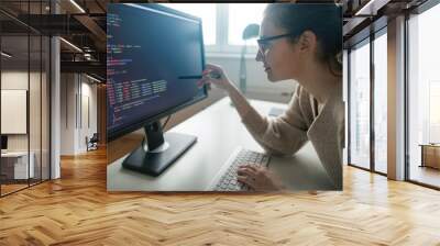 Young woman programming at her home office. Female programmer ponting at computer codes Wall mural