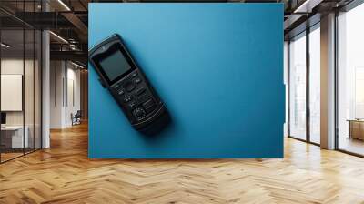 A black remote control resting on a blue surface in a well-lit setting Wall mural