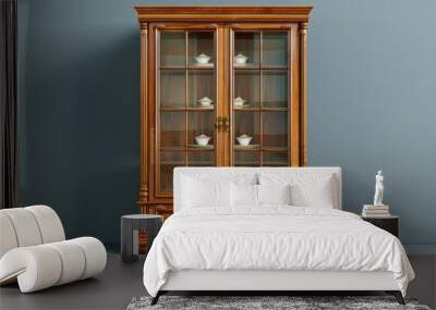 Elegant wooden display cabinet showcasing porcelain items against a blue wall Wall mural