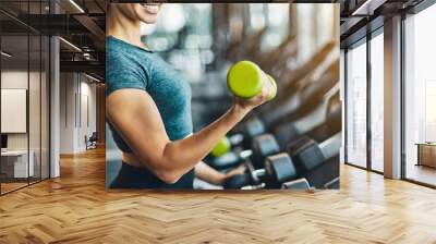 fitness woman demonstrates dumbbell exercises, showcasing determination and strength in a vibrant gym setting Wall mural