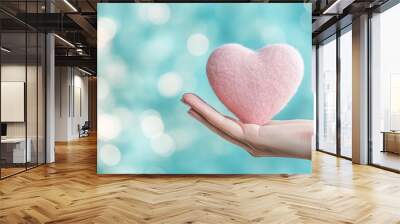 hand gently holds a 3D heart against a blurred background, symbolizing love, care, and compassion. The empty space invites interpretations of hope and emotional connection Wall mural