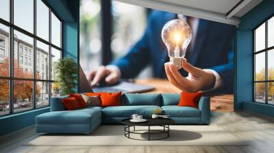 Hand holding a glowing lightbulb symbolizing creativity and business ideas Wall mural