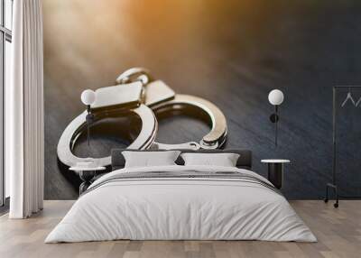 Handcuffs on dark table, symbolizing confinement and control. Dark background with backlighting, suggestive of secrecy and constraint Wall mural