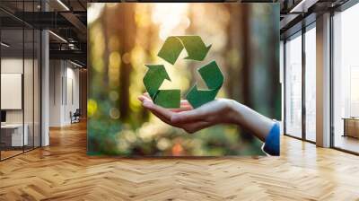 hands hold a green recycle symbol against a sunlit forest background, symbolizing environmental protection, sustainability, and the importance of recycling Wall mural