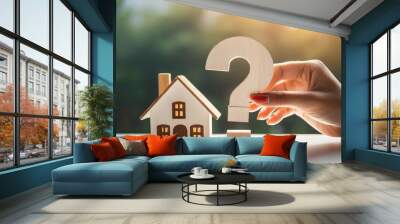 woman's hand holds 3D question mark beside wooden house, symbolizing real estate inquiries Wall mural