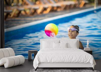 A girl in a bright bathing suit swims with an inflatable ball in a pool with clear water on a summer evening Wall mural