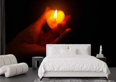 A hand holding a burning candle in the shape of a heart. Dark background. Wall mural