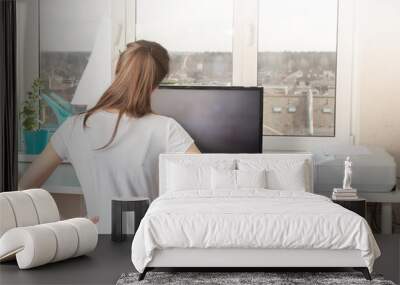 Doing sports at home. Young woman doing exercises looking at the monitor Wall mural