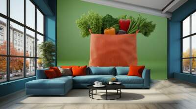 A vibrant orange bag filled with fresh vegetables against a green background, showcasing healthy food options. Wall mural