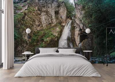 A waterfall falls from a cliff in the jungle among the green vegetation. spring melting of glaciers Wall mural