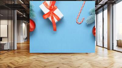 Beautiful Christmas banner. Gift box, candy cane and decorative spruce branch with red ball on a blue paper background. Top view, flat lay. Wall mural