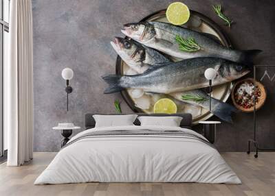 Flat lay fresh raw fish seabass in a plate with ice cubes, rosemary and lime on a dark rustic background. Top view, copy space. Wall mural