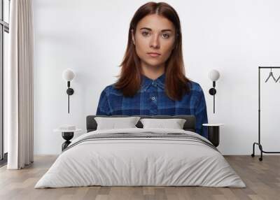 Horizontal shot of serious mixed race attractive self assured young woman with specific appearance, looks directly at camera, ready for conversation, dressed in blue checkered shirt, isolated indoors. Wall mural