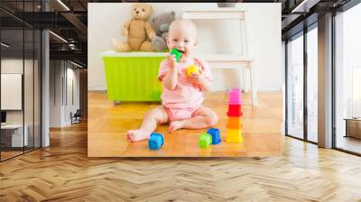 Little baby girl sitting on the floor, crawling and playing with brightly colored educational toys Wall mural