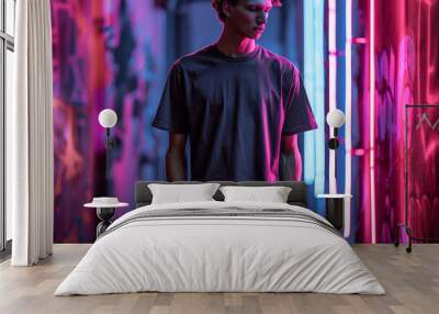 Mock up t-shirt. A man wearing a black t-shirt stands in an urban setting, illuminated by vibrant neon lights. This image is ideal for showcasing your designs and capturing a modern, edgy vibe. Wall mural