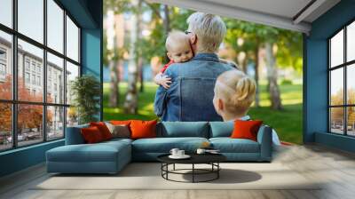 caucasian blond haired woman carry baby daughter. Schoolboy son looking at little sister Wall mural