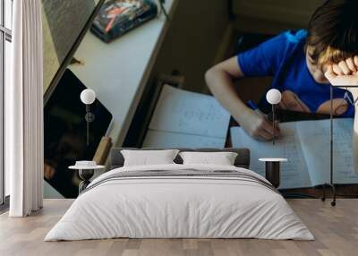 stressed tired boy doing homework at home at the desk by the window. Wall mural