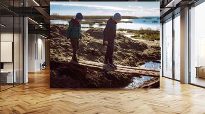 two caucasian 607 years old boys crossing the stream over handmade bridge made of wooden planks. Sunny october day on the sea shore. Image with selective focus and backlight Wall mural