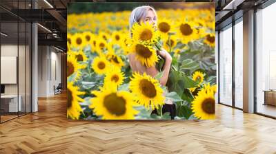 A beautiful young woman with bare shoulders smiles in a sunflower field. The theme of cosmetology, skin care, vacation and relaxation in a calm atmosphere. Wall mural