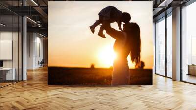 A mother lifts a toddler child in the air above a picturesque sunset sky. A woman and a little girl in a field of lavender flowers. Copy space Wall mural