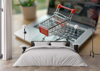 An overhead shot of a miniature shopping cart next to a laptop, symbolizing online shopping and digital marketplace. Wall mural