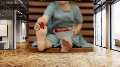 Baby girl eating raspberry on picnic and put on feet. Wall mural