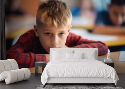 Bored schoolboy do task tired exhausted upset fatigued unmotivated little child boy kid pupil schoolchild lying on table desk writing homework boring class lesson education learning problems school Wall mural