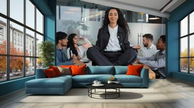 Calm businesswoman leader woman doing breathing yoga exercise taking break meditating sitting at table in office in meditation background meeting business colleagues discussing project brainstorming Wall mural