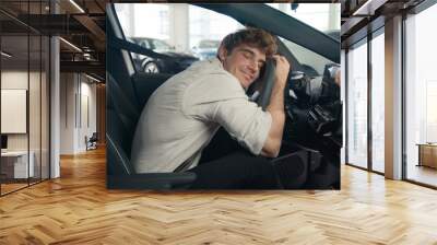 Caucasian client man buyer guy customer male sitting in luxury new car choosing auto visit showroom choose automobile rent test drive buying enjoy vehicle choice embrace hug cuddling wheel steering Wall mural