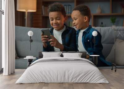 Children gadget addiction two happy laughing African American little boys brothers browsing mobile phone watching cartoons online without parental control at home couch kids siblings using smartphone Wall mural